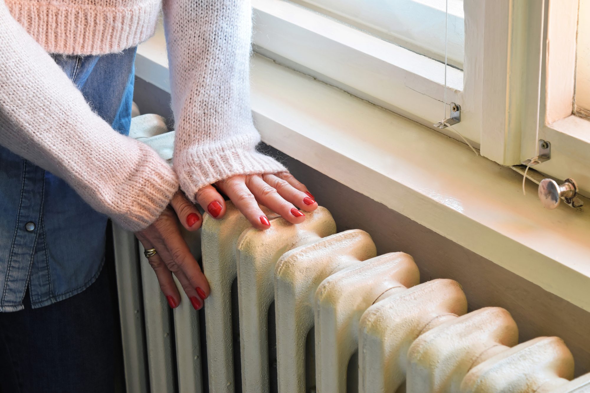 Home central heating system, woman`s hands on an old and robust metal radiator.